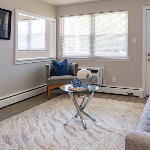 Spacious and well lit living room with wood floors and a large window with access to the kitchen